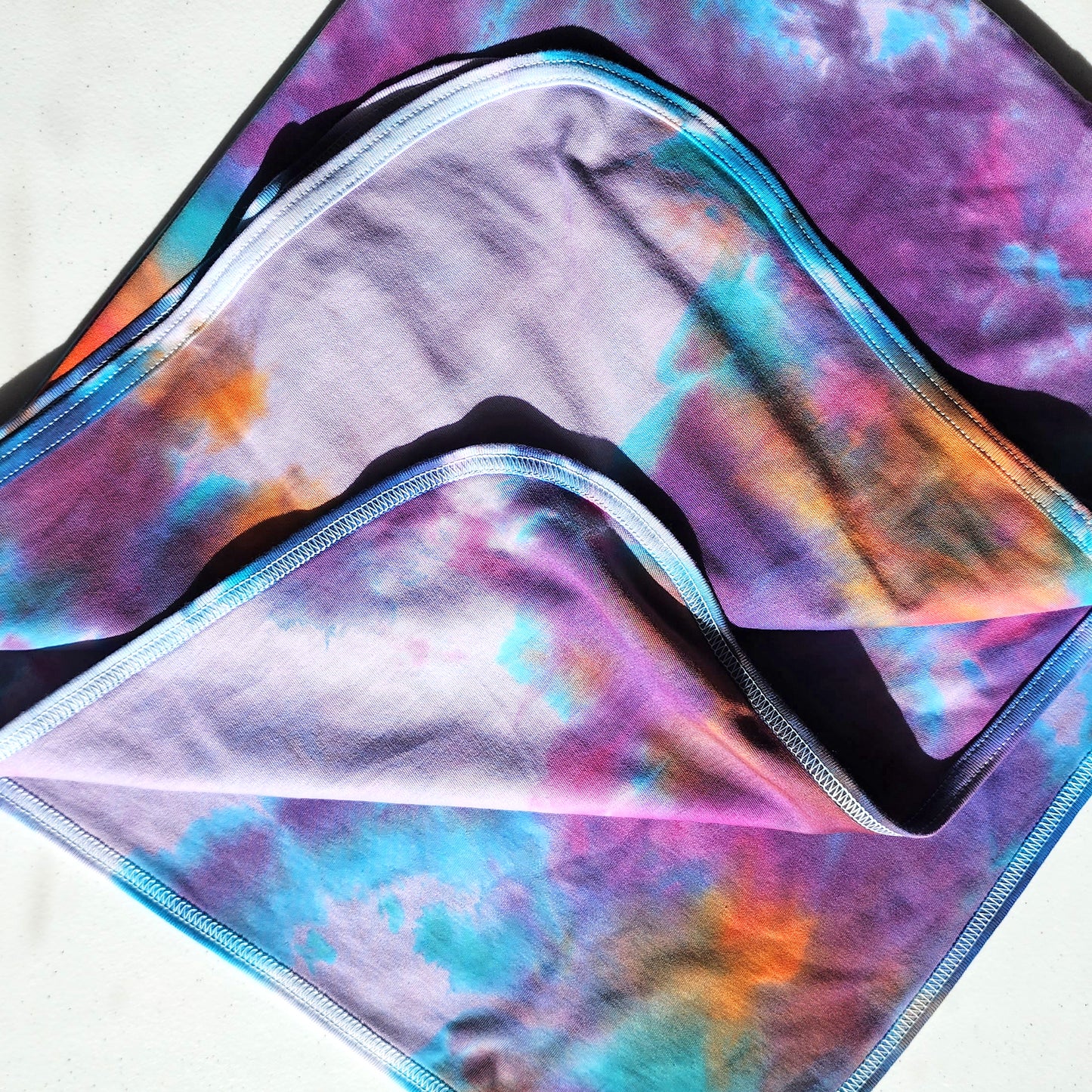 Colorful tie dye baby blanket on a beige background.