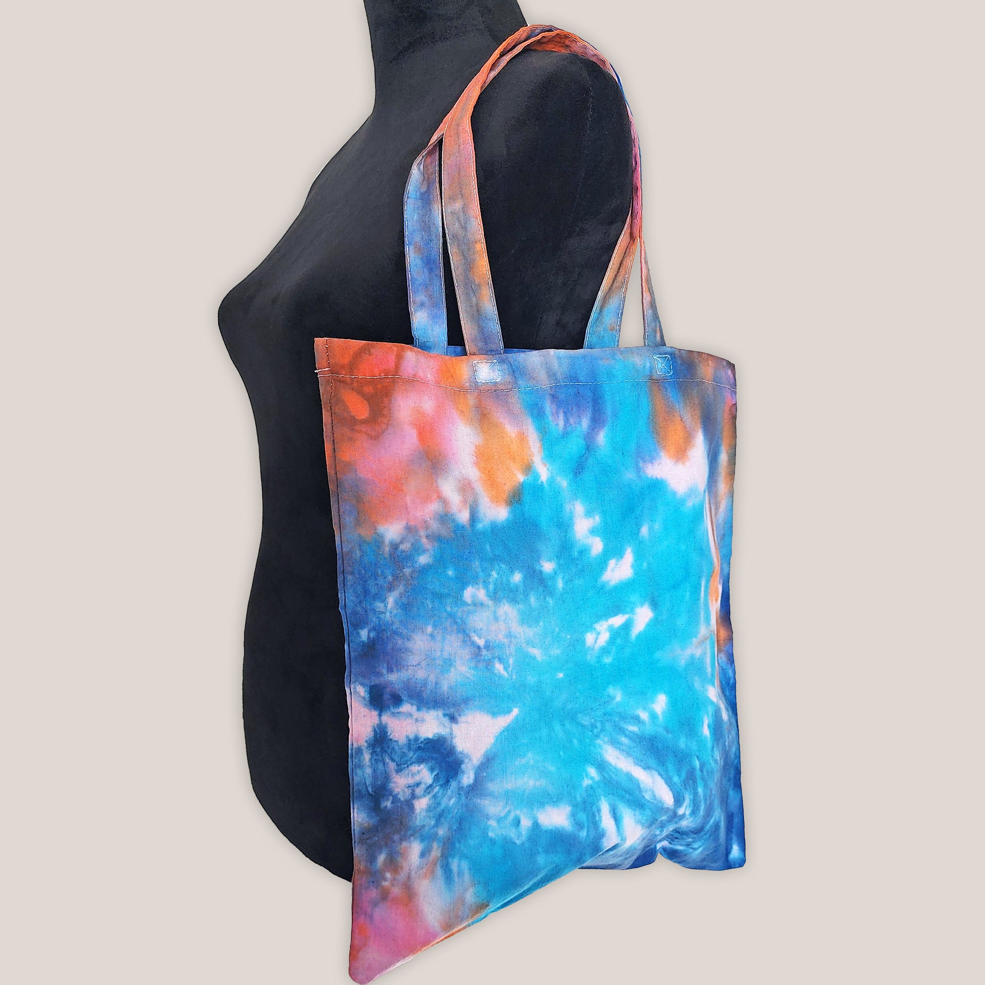 Tie dye tote bag on a black mannequin with a beige background.
