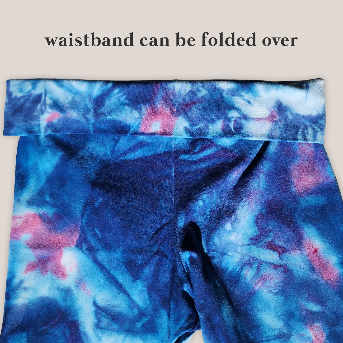 Blue tie-dye pants with a waistband that can be folded over on a beige background.