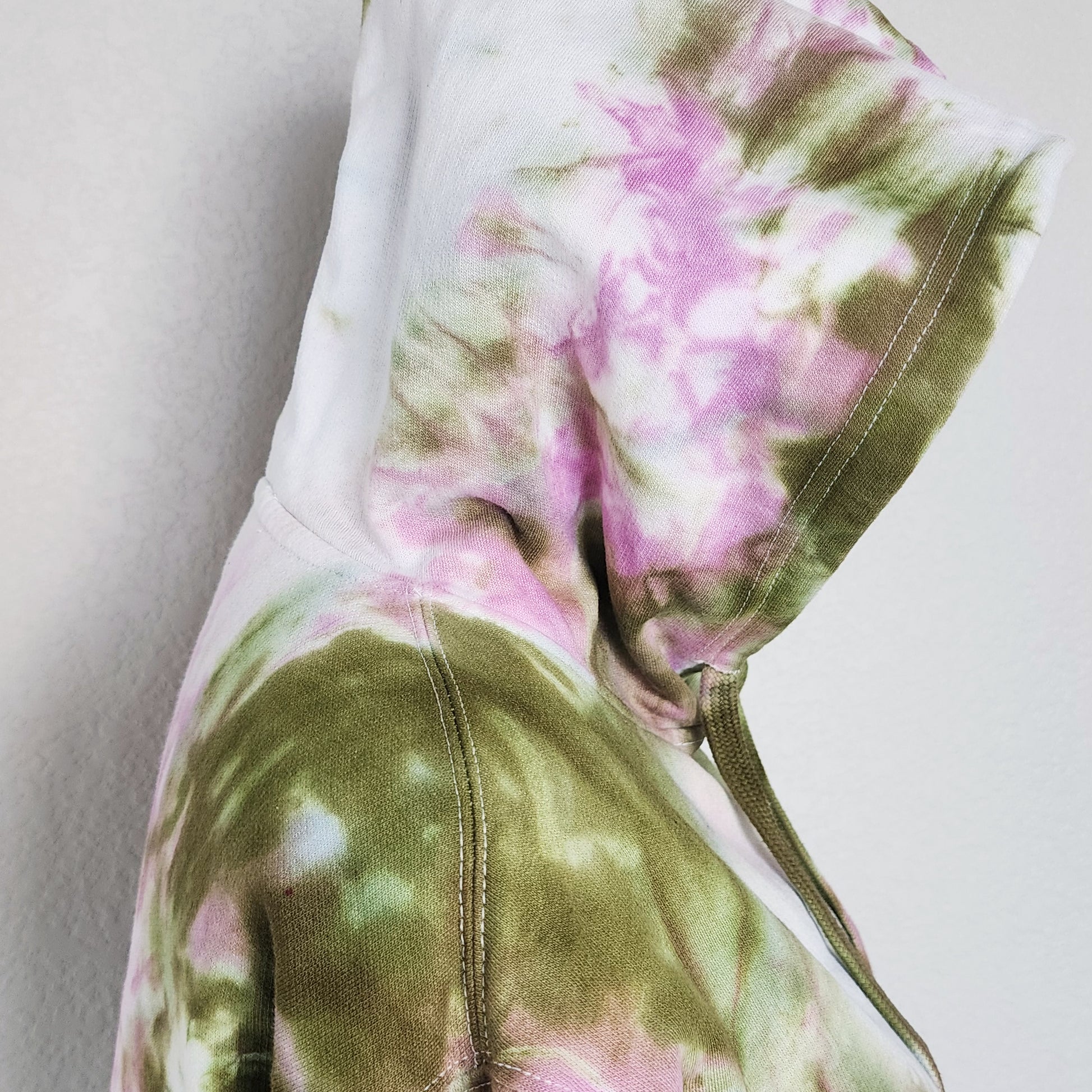 Close-up of a tie-dye hoodie with pink and green patterns on a plain background