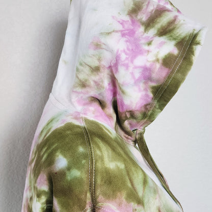 Close-up of a tie-dye hoodie with pink and green patterns on a plain background