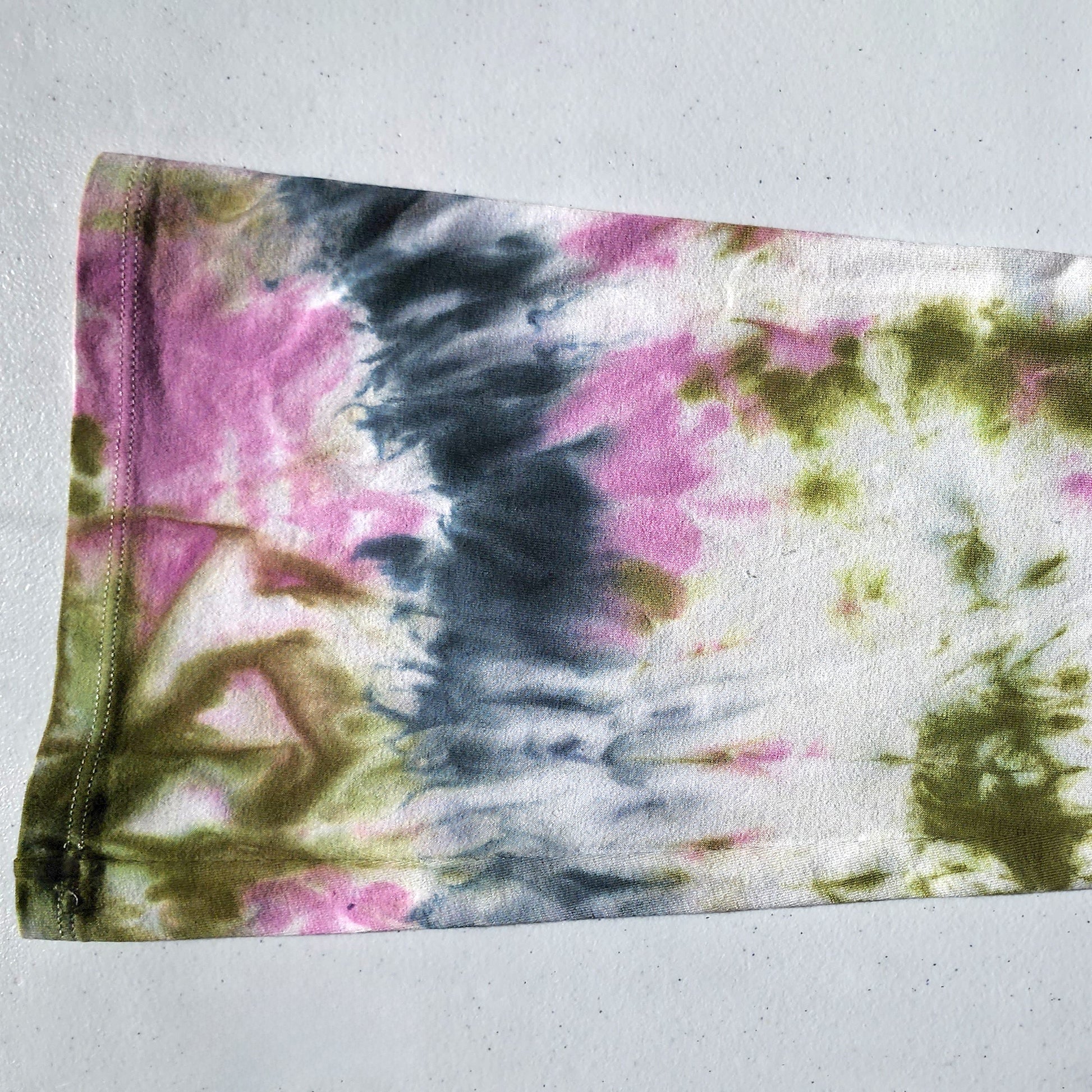 Tie-dye fabric with pink, green, and black patterns on a white background