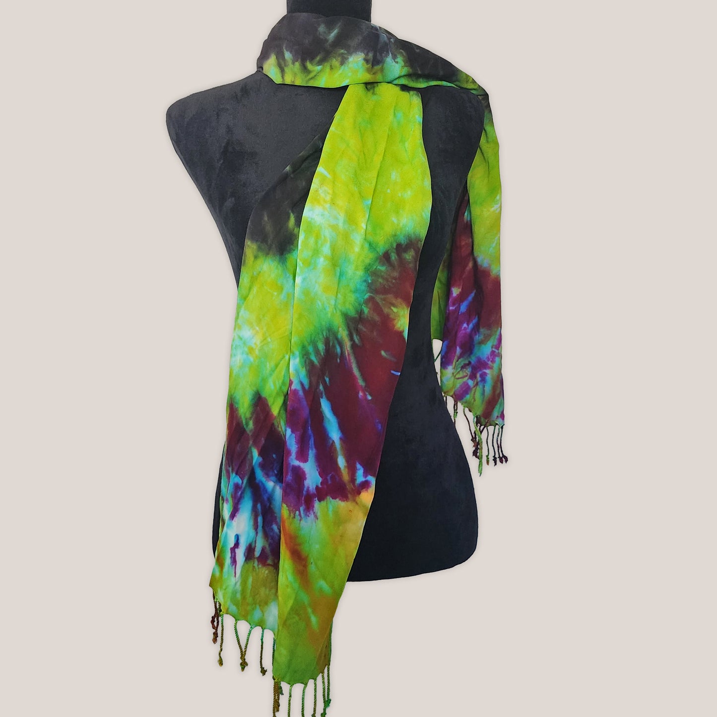Tie-dye scarf with green, purple, and black colors on a mannequin against a plain background