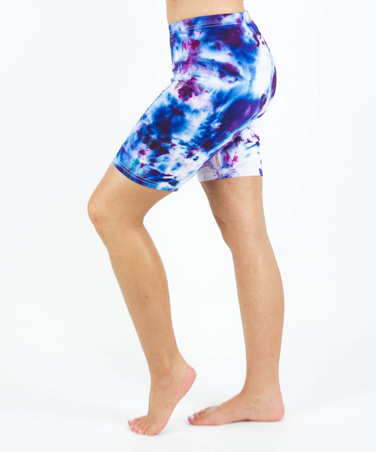 Woman wearing Akasha Sun ice dye tie-dye biker shorts in the colors purple, blue, and white.