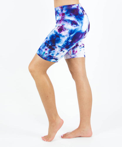 Woman wearing Akasha Sun ice dye tie-dye biker shorts in the colors purple, blue, and white.