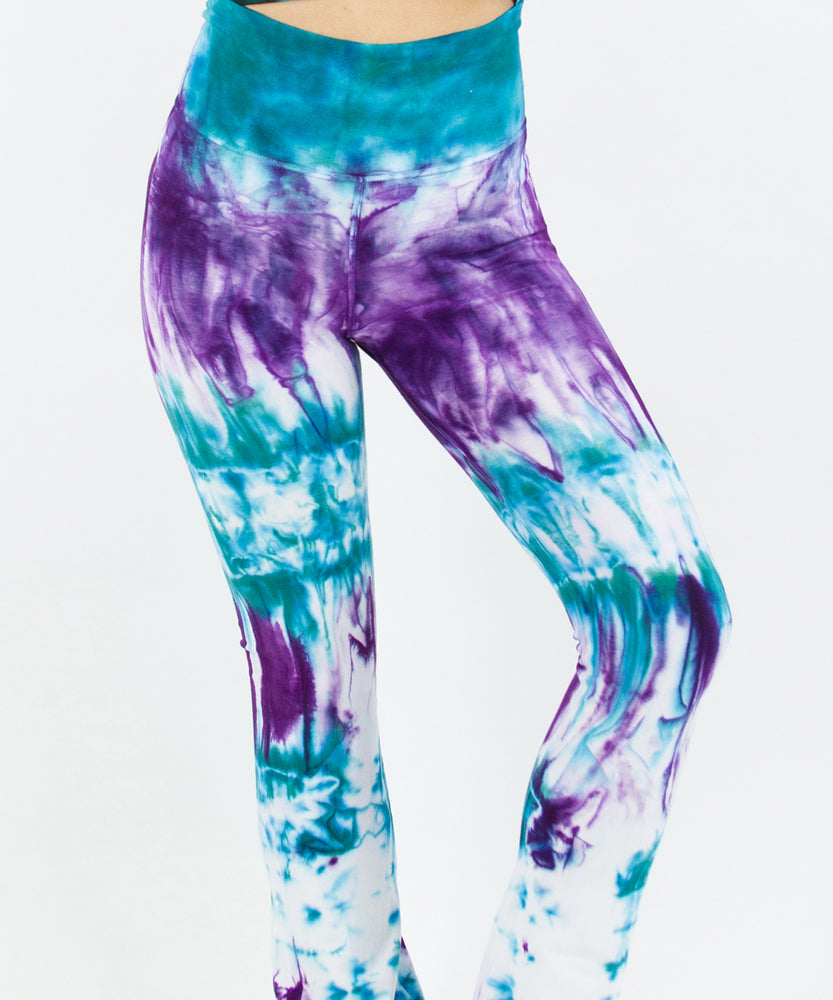 Woman wearing a pair of teal and purple tie dye yoga pants featuring a fold over waistband.