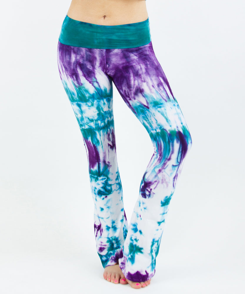 Woman wearing a pair of teal and purple tie dye yoga pants featuring a fold over waistband.