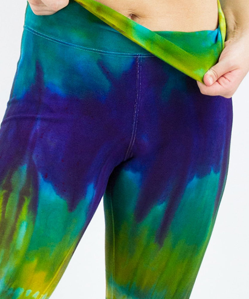 Woman wearing a navy blue and green tie dye yoga pants featuring a fold over waistband.