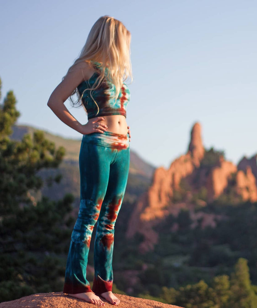 
                
                    Load image into Gallery viewer, Woman standing in Garden of the Gods wearing Kiowa tie dye yoga pants with a fold over waistband in the colors teal and copper.
                
            