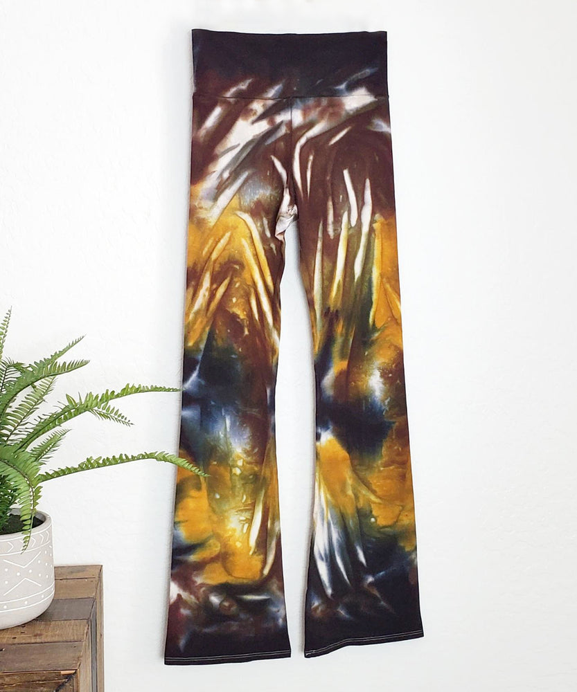 A pair of tie dye yoga pants with a wide waistband in the color amber, brown, and black.