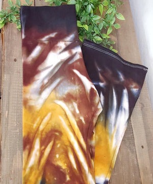 A pair of tie dye yoga pants with a wide waistband in the color amber, brown, and black.