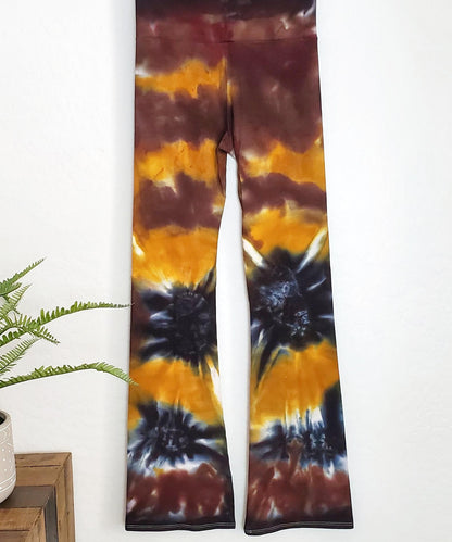 A pair of tie dye yoga pants with a wide waistband in the color amber, brown, and black.