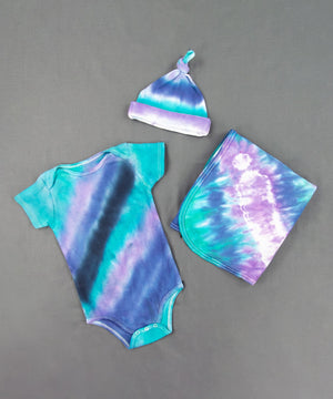 Teal, purple, and black tie dye baby set that includes a baby hat, bodysuit, and baby blanket.