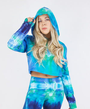 
                
                    Load image into Gallery viewer, Woman wearing the Galapagos Islands Tie Dye Hoodie Crop Top.  The colors of the crop top include navy blue, teal, aqua, and blue.  Featuring a hood, drawstrings, and raw edge.
                
            
