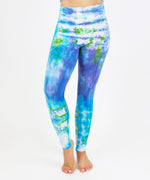 Woman wearing the Grenada tie dye leggings that feature a fold over waistband.  The colors of the leggings include aqua, lavender, and emerald.