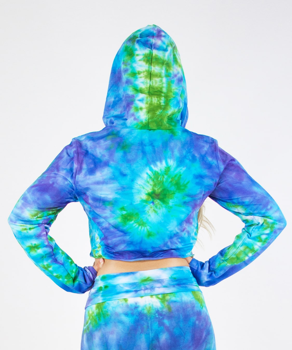 Woman wearing the Grenada tie dye hoodie crop top featuring hand-dyed hues of aqua, purple, and green.