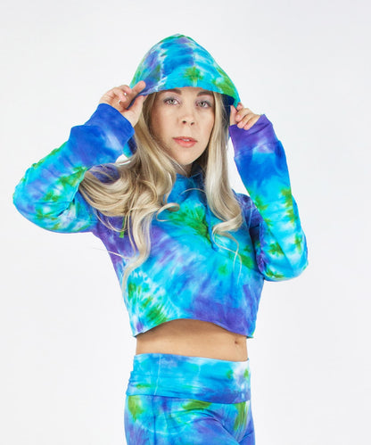 Woman wearing the Grenada tie dye hoodie crop top featuring hand-dyed hues of aqua, purple, and green.