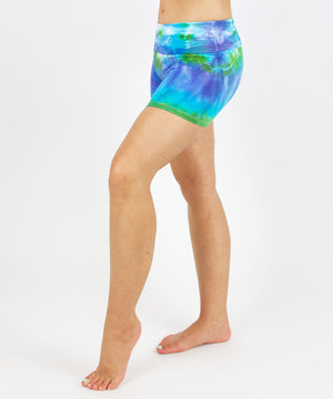 Woman wearing the Grenada tie dye shorts featuring a fold over waistband.  The colors in the shorts include blue, purple, and green.