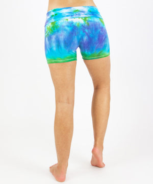 Woman wearing the Grenada tie dye shorts featuring a fold over waistband.  The colors in the shorts include blue, purple, and green.