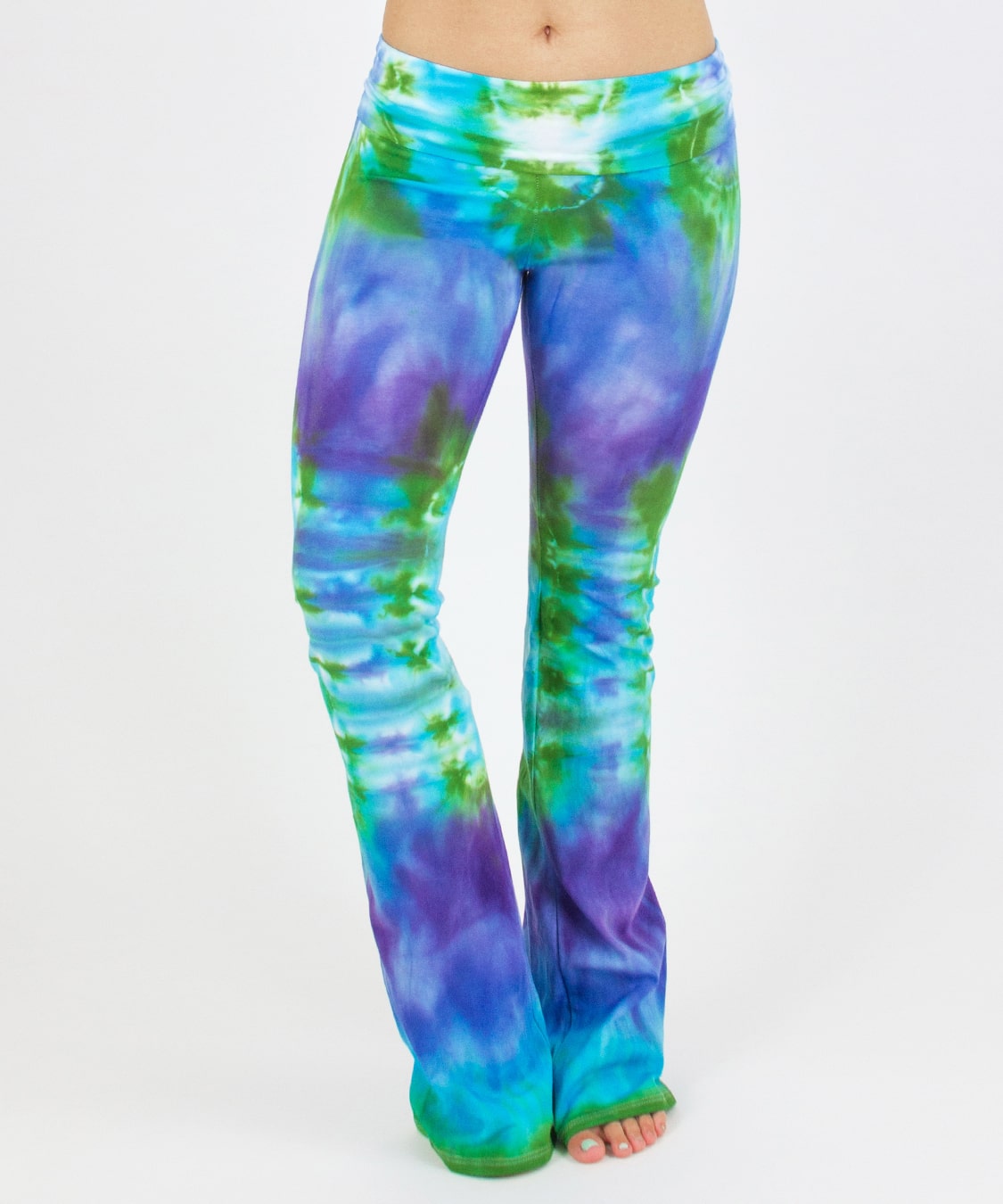 Woman wearing the Grenada tie dye yoga pants that feature a fold over waistband.  The pants have the colors aqua, purple, and green.