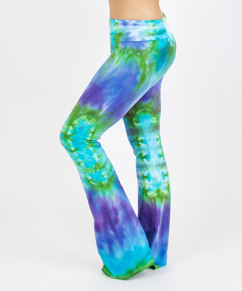 Woman wearing the Grenada tie dye yoga pants that feature a fold over waistband.  The pants have the colors aqua, purple, and green.