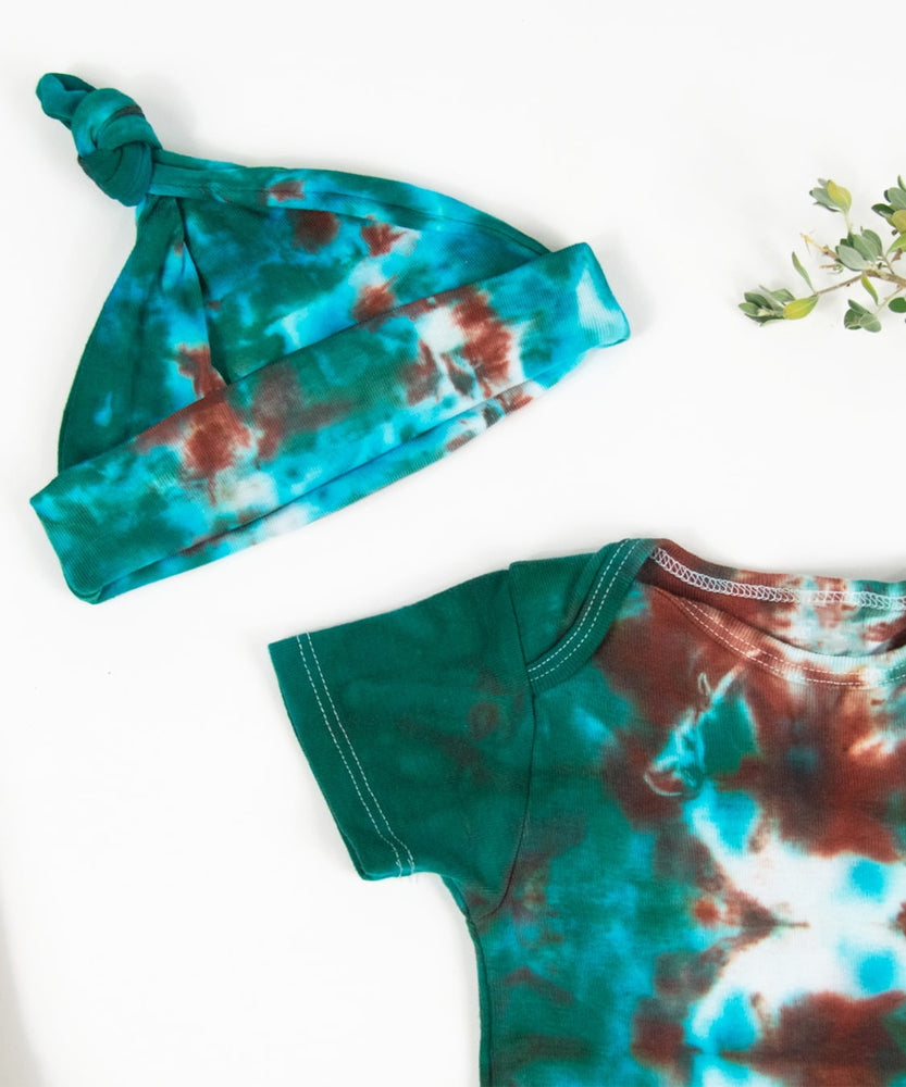 A teal and copper tie dye onesie and baby hat set by Akasha Sun.