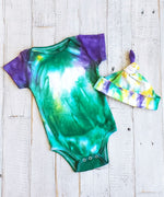 An organic tie dye baby bodysuit and hat in Mardi Gras colors of green, purple, and yellow.