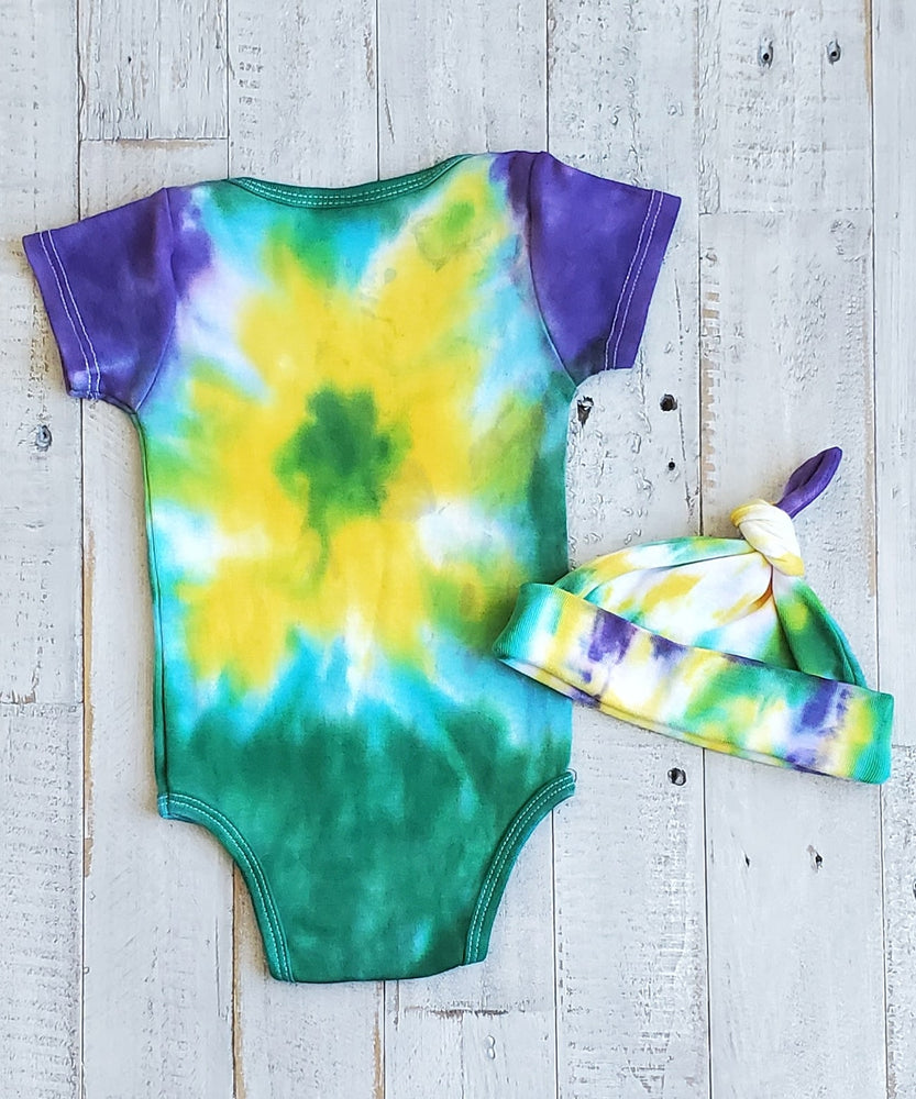 An organic tie dye baby bodysuit and hat in Mardi Gras colors of green, purple, and yellow.