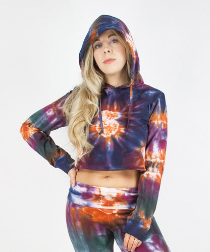 Woman wearing the Meteor tie dye hoodie crop top that features a hood, drawstrings, and raw edge.  The colors in the crop top include orange, navy, purple, and green.