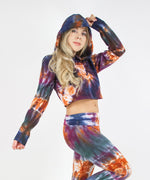 Woman wearing the Meteor tie dye hoodie crop top that features a hood, drawstrings, and raw edge.  The colors in the crop top include orange, navy, purple, and green.