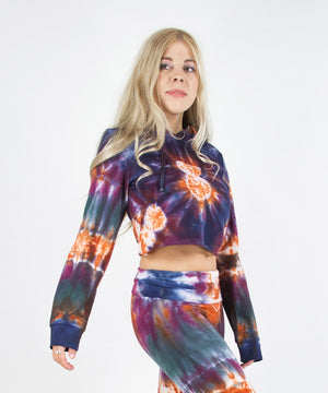 Woman wearing the Meteor tie dye hoodie crop top that features a hood, drawstrings, and raw edge.  The colors in the crop top include orange, navy, purple, and green.
