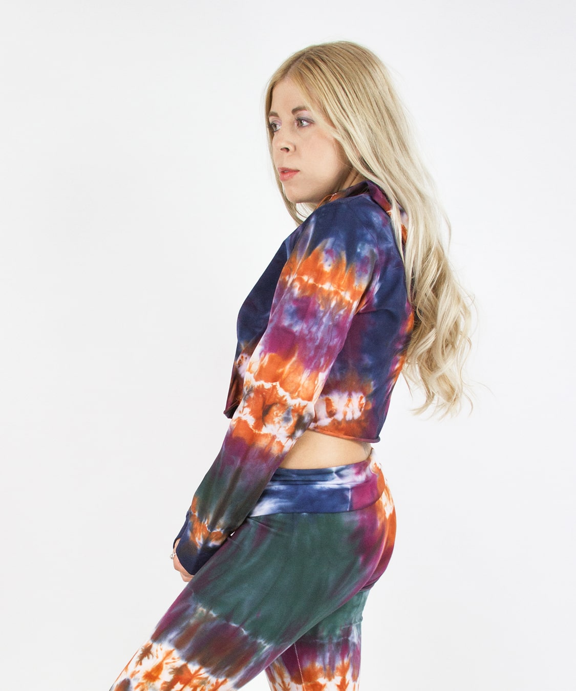 Woman wearing the Meteor tie dye hoodie crop top that features a hood, drawstrings, and raw edge.  The colors in the crop top include orange, navy, purple, and green.