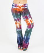 Woman wearing the Meteor tie dye yoga pants that feature a fold over waistband.  The colors in these pants include orange, purple, green, and navy blue.