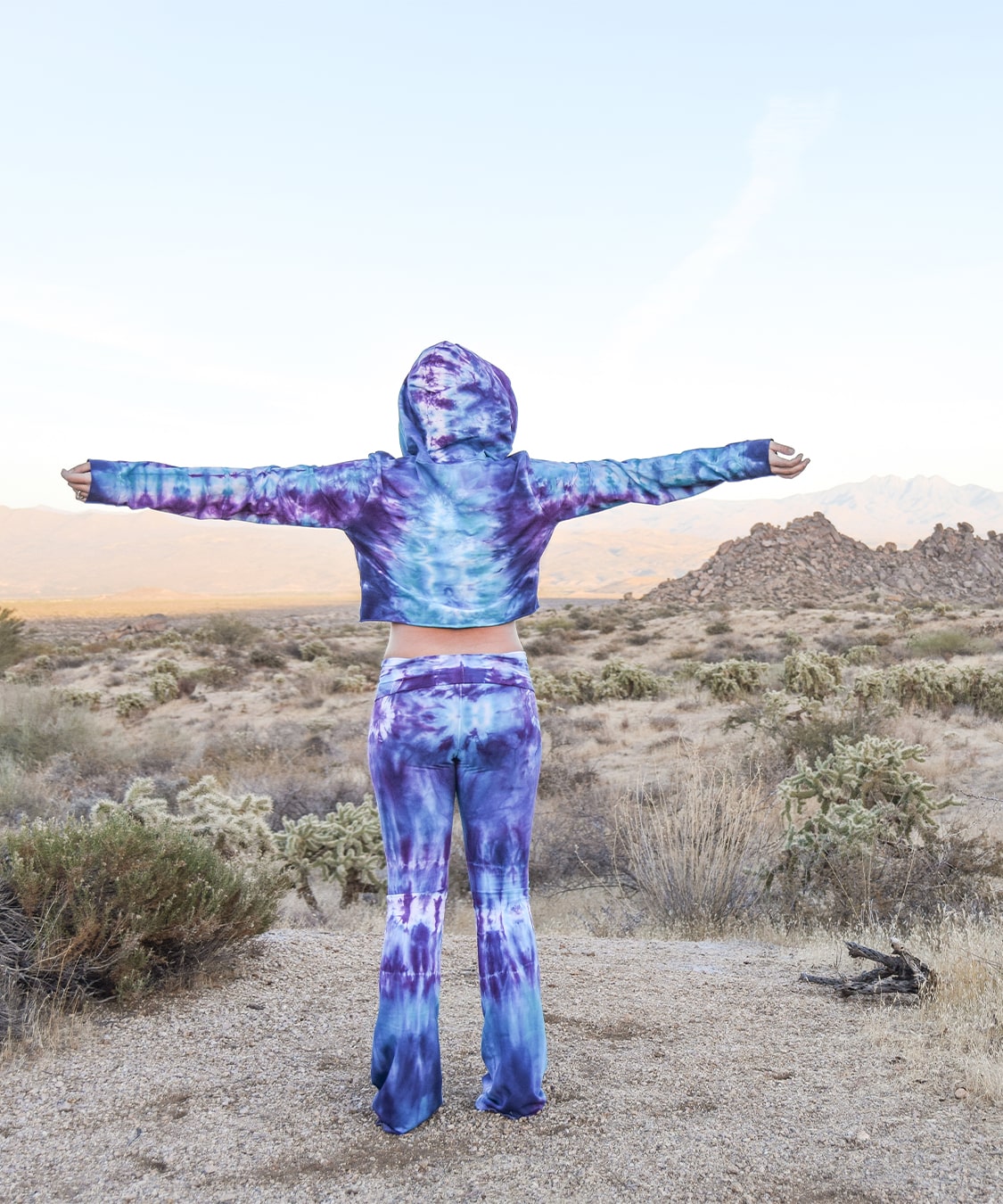 Woman wearing a pair of tie dye yoga pants and hoodie crop top.