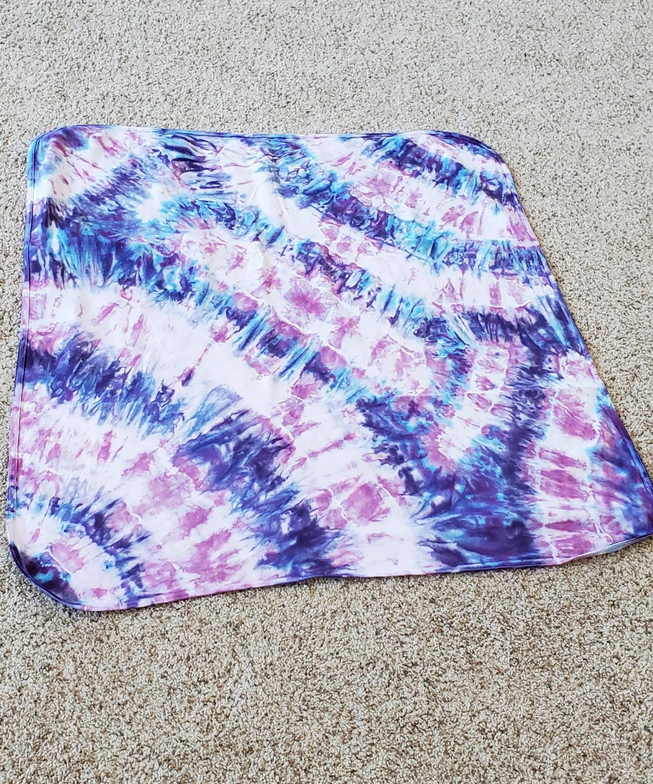 A purple and pink tie dye organic baby blanket with rounded corners.