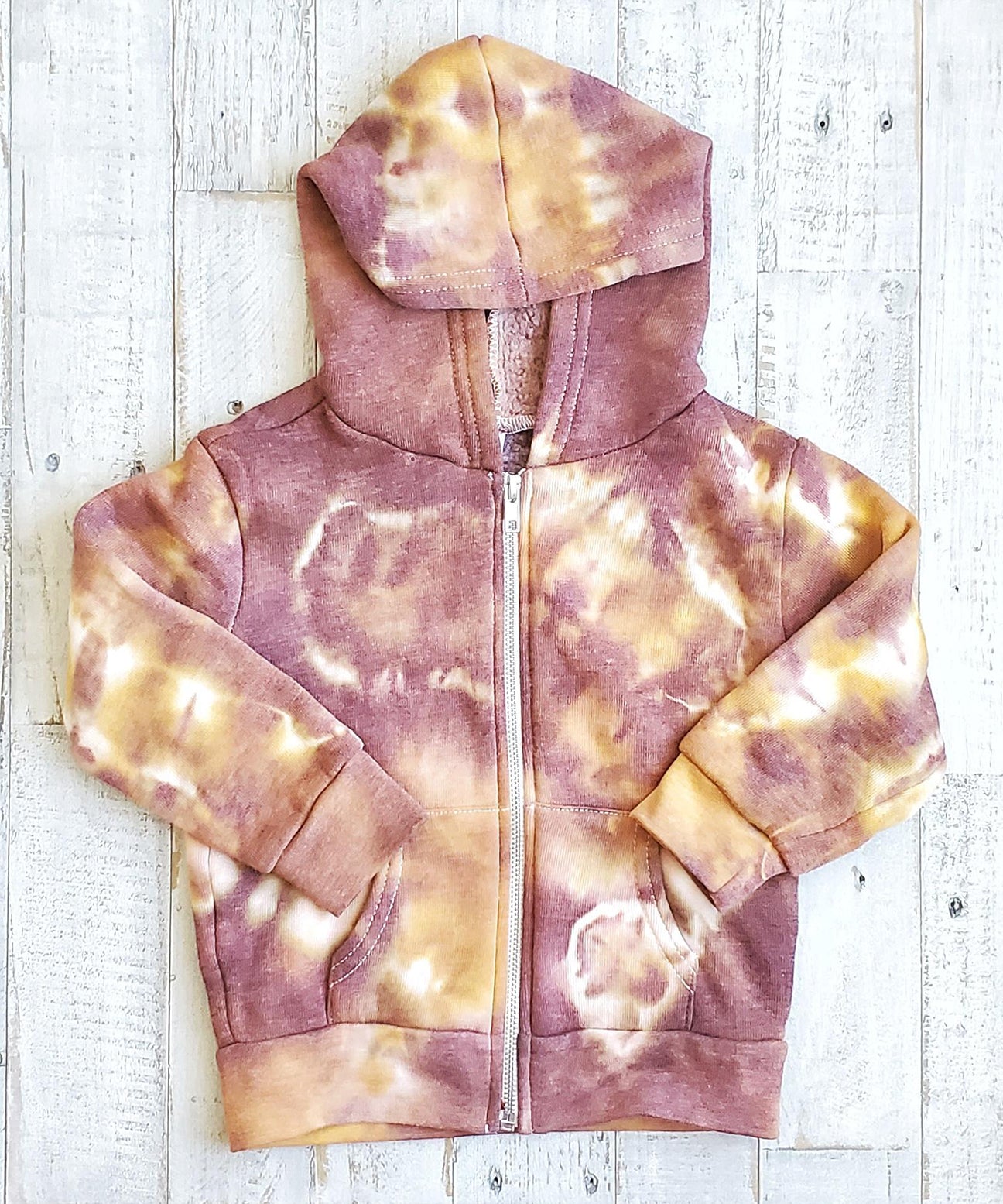 A rust tie dye children's jacket with fleece lining, pockets, and hood.