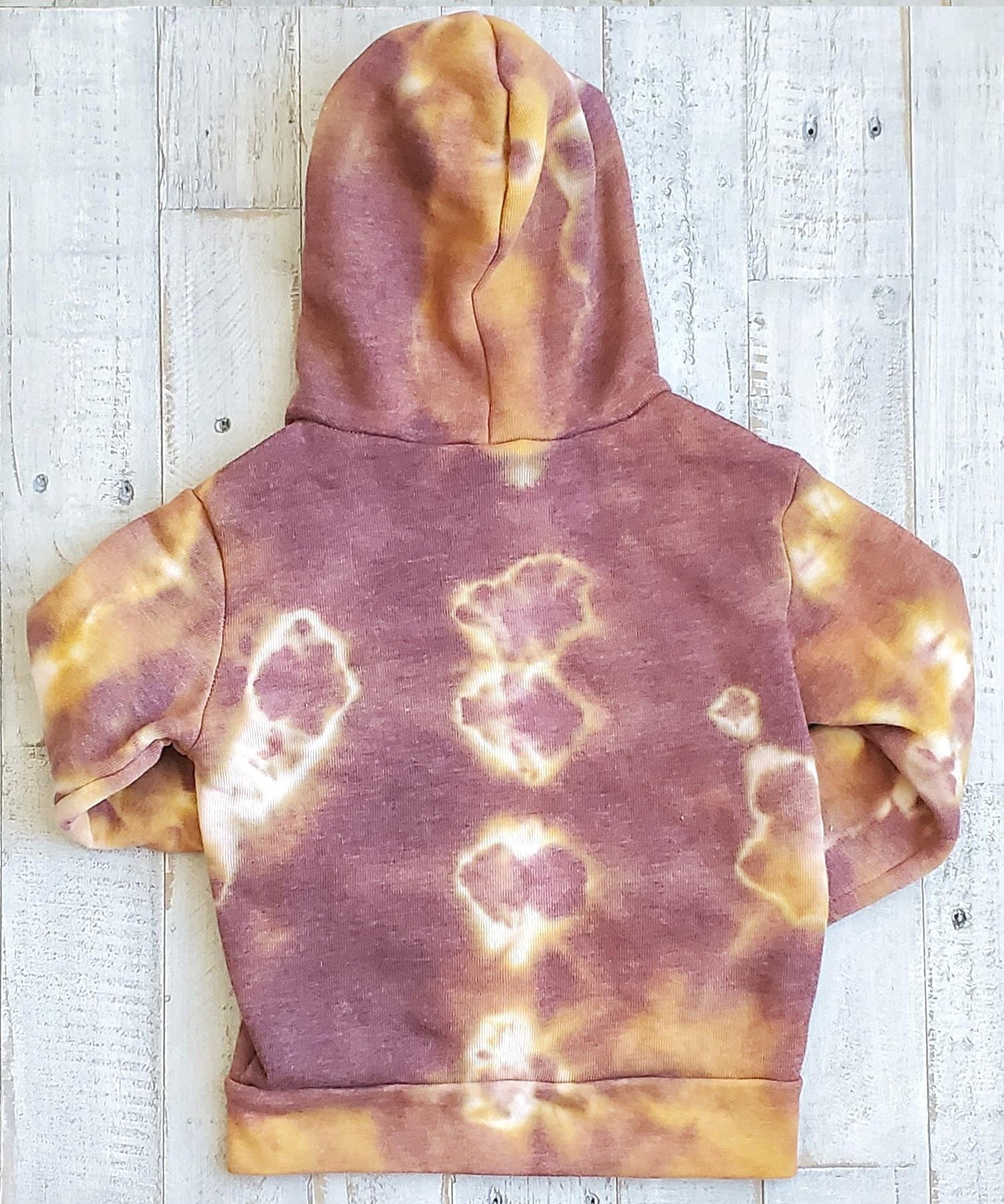 A rust tie dye children's jacket with fleece lining, pockets, and hood.