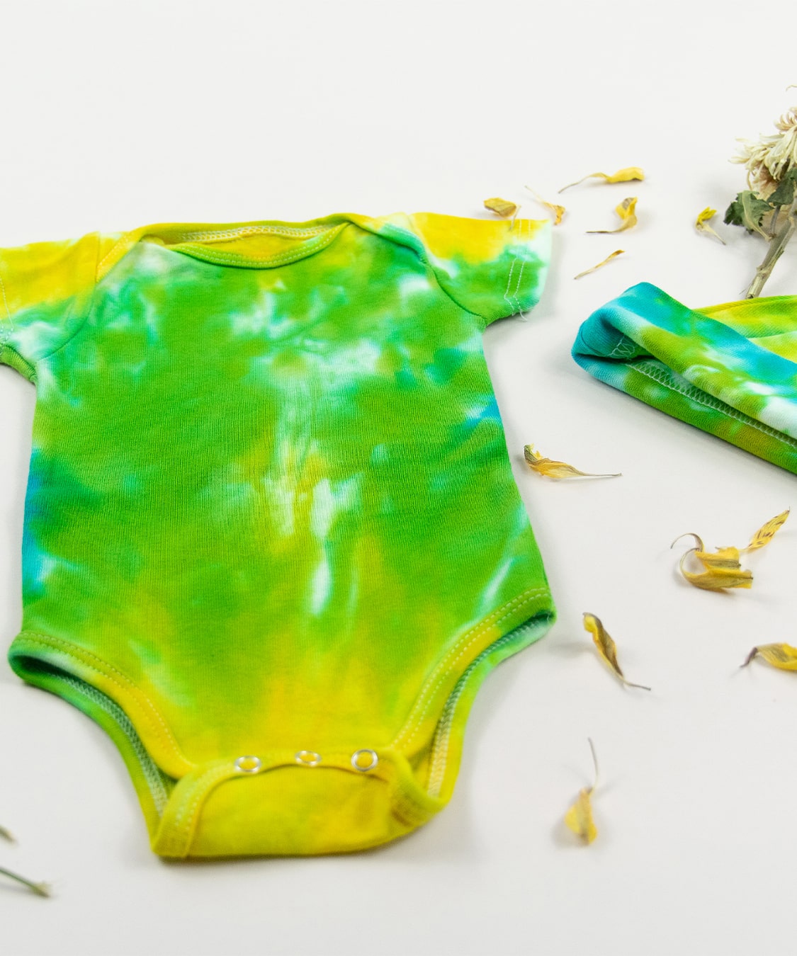 Green, yellow, and blue tie dye organic cotton baby bodysuit and hat set by Akasha Sun.