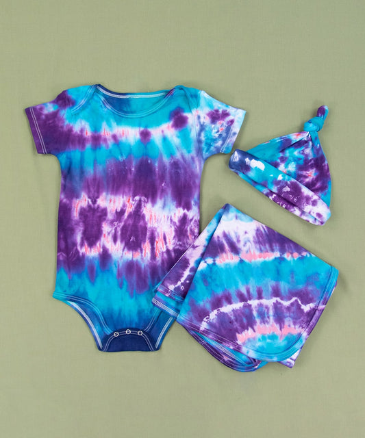 Blue, purple, and pink tie dye baby set that includes a bodysuit, hat, and baby blanket.