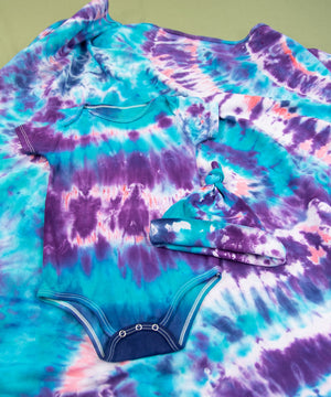 Blue, purple, and pink tie dye baby set that includes a bodysuit, hat, and baby blanket.