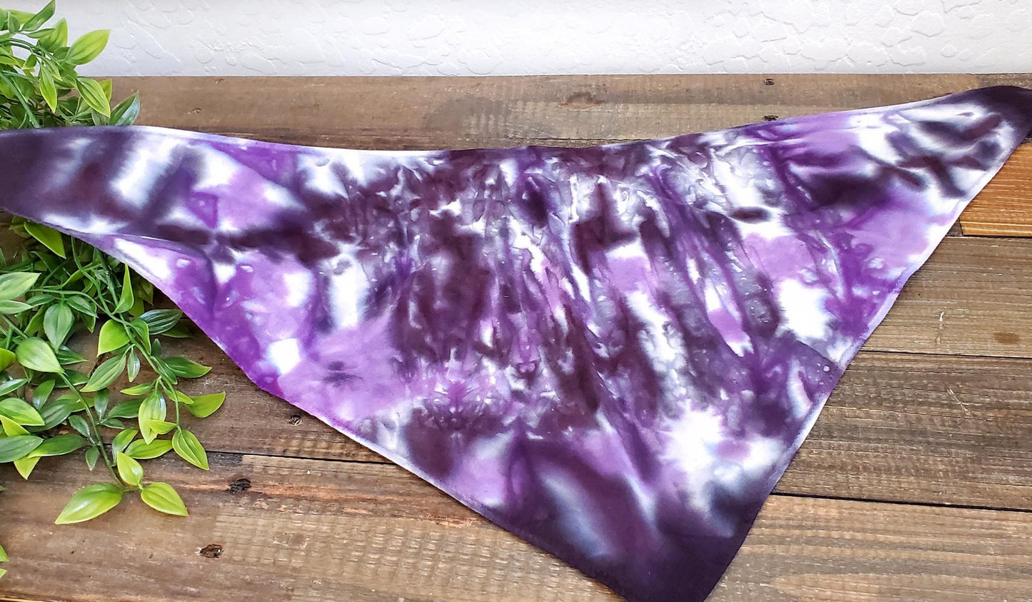 A dog modeling a tie dye dog bandana in the colors purple and black.