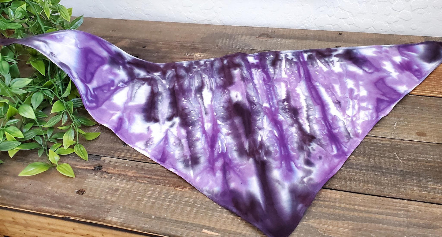 A dog modeling a tie dye dog bandana in the colors purple and black.